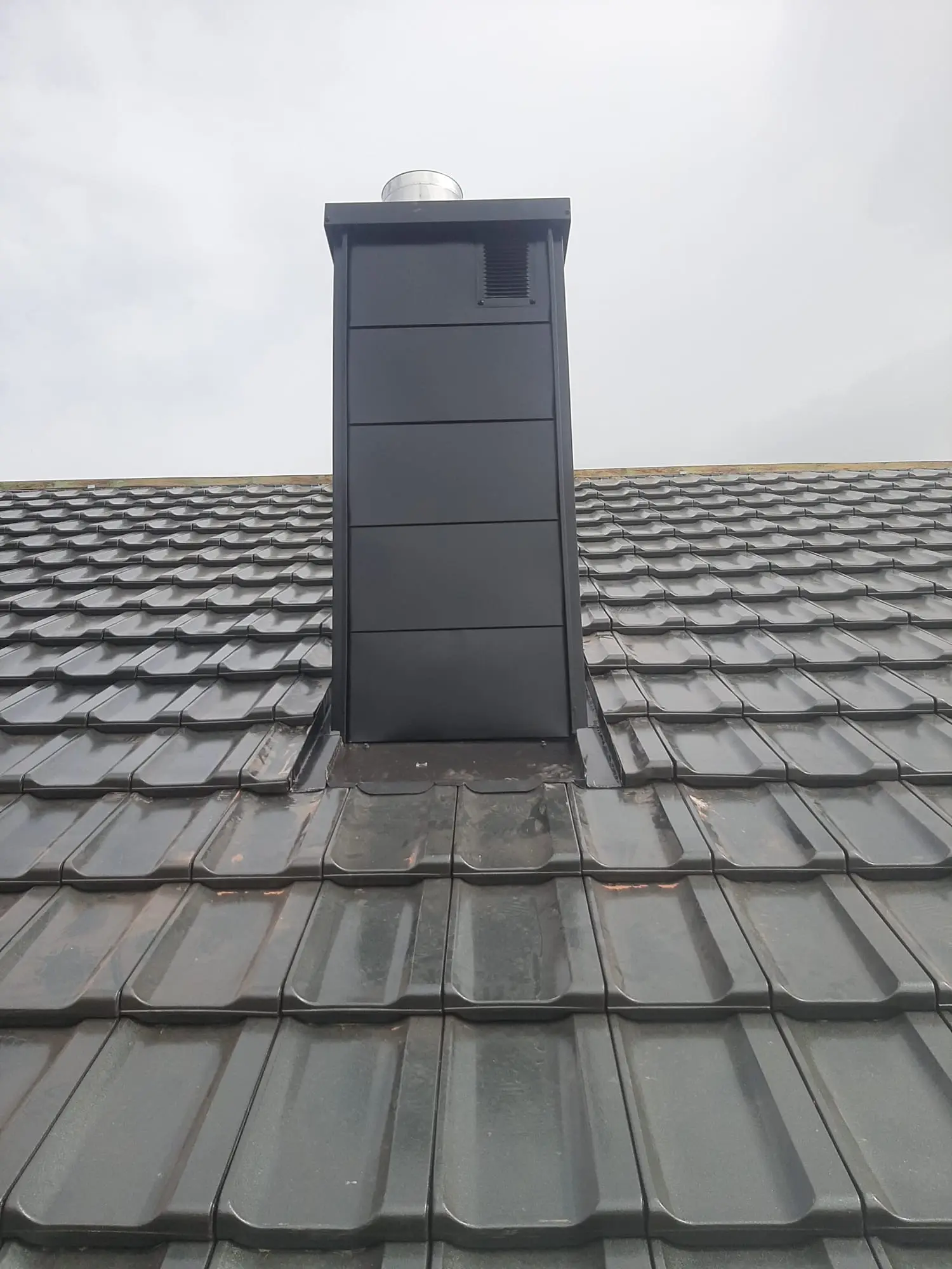 Obróbka blacharska komina z dokładnym wykończeniem przy połaci dachowej